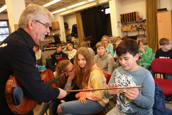 Ein Musiker zeigt Kindern seinen Geigenbogen